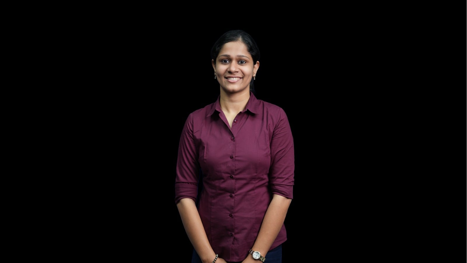 Anuthama_BSF_IDA Smiling woman in a burgundy button-up shirt stands against a black studio background.